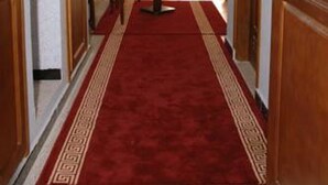 A hotel corridor with a red carpet, wooden doors, and a view of a room with a bed and curtains. - Majestic Annaba (Annaba)