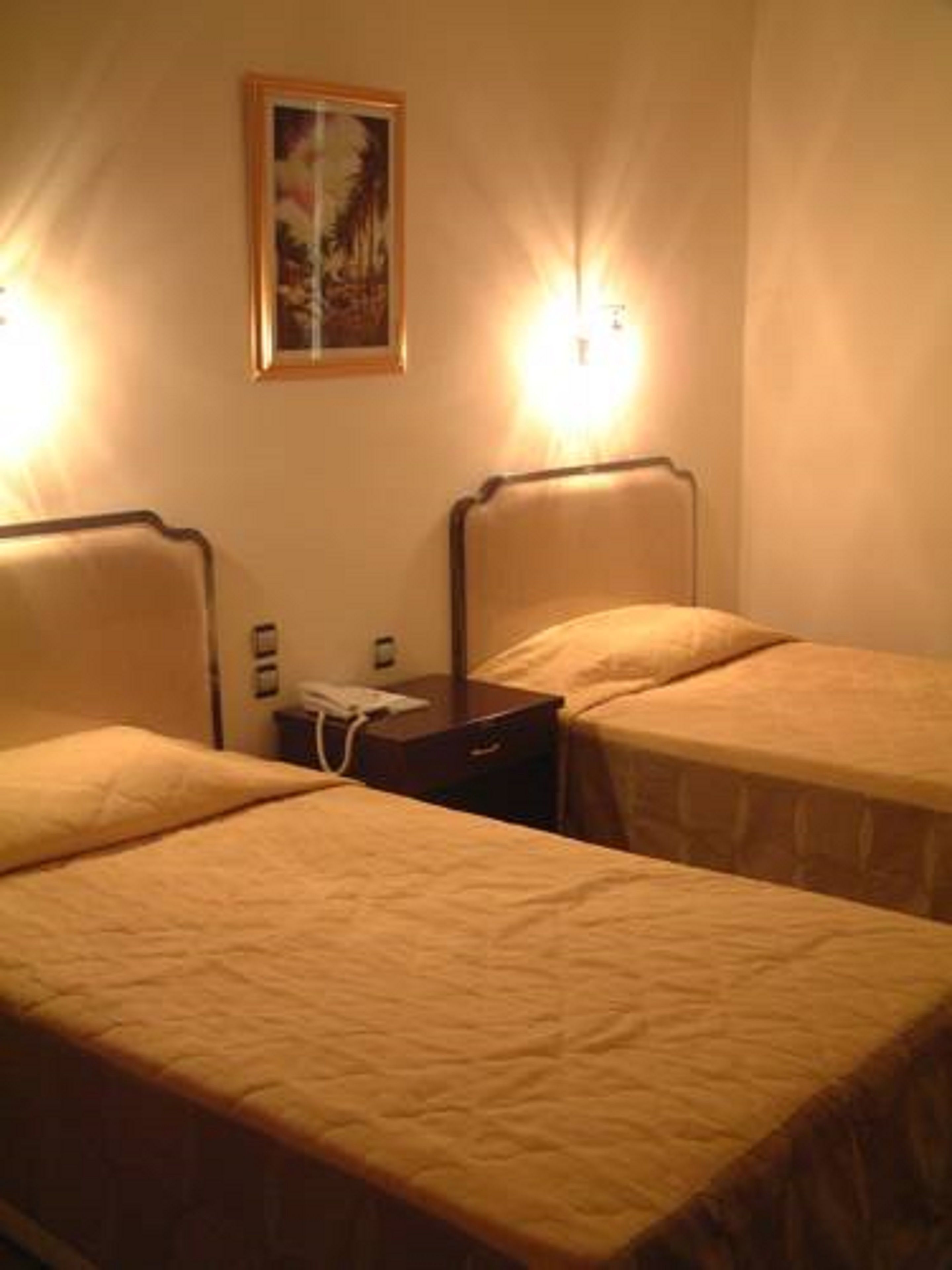Una habitación de hotel con dos camas individuales, una mesita de noche, un teléfono y un cuadro en la pared.
