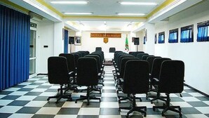 A hotel lobby with a checkered floor, rows of black office chairs, a reception desk, and a flag on the wall. - Majestic Annaba (Annaba)
