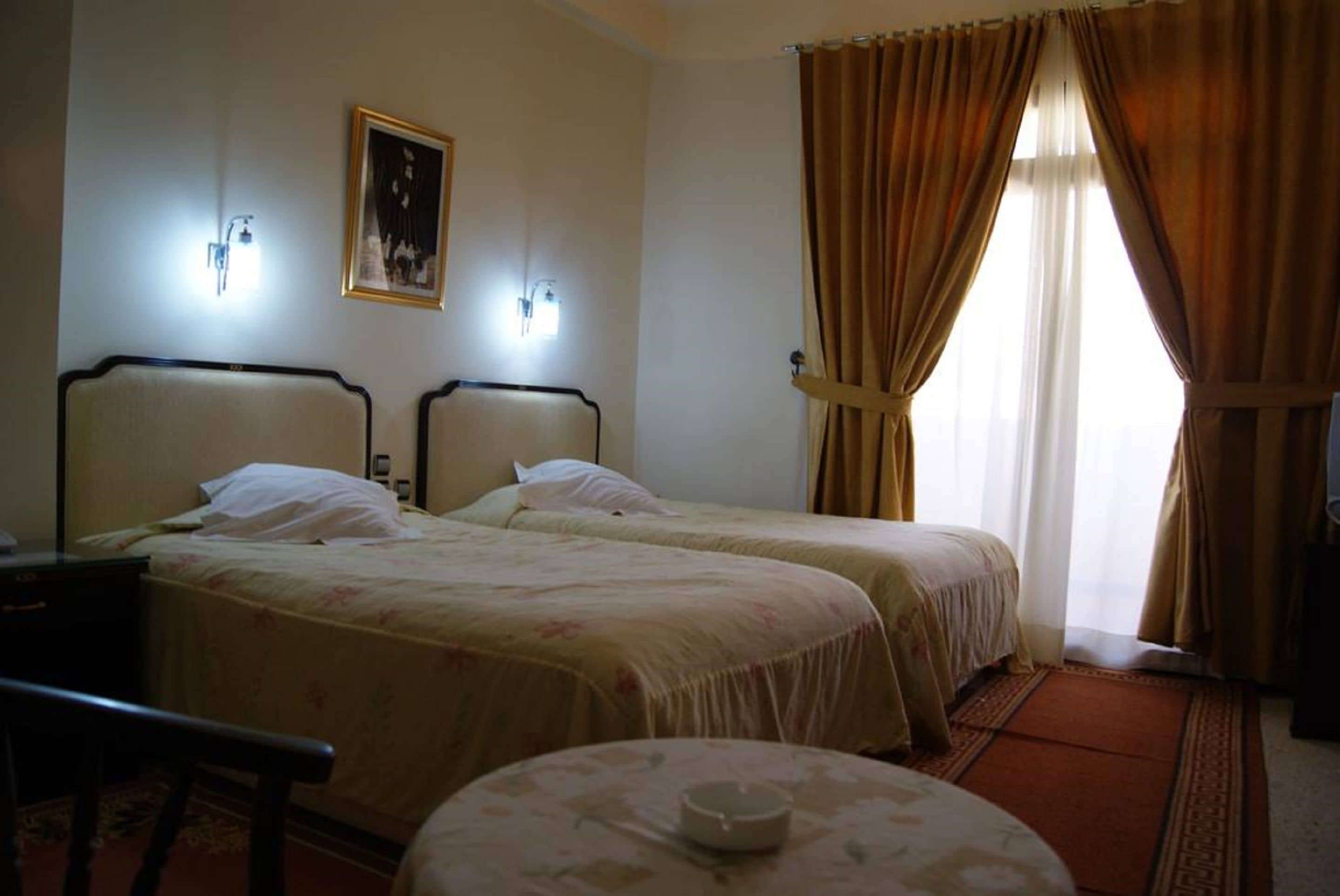 A hotel room with two beds, a small table, and a chair.