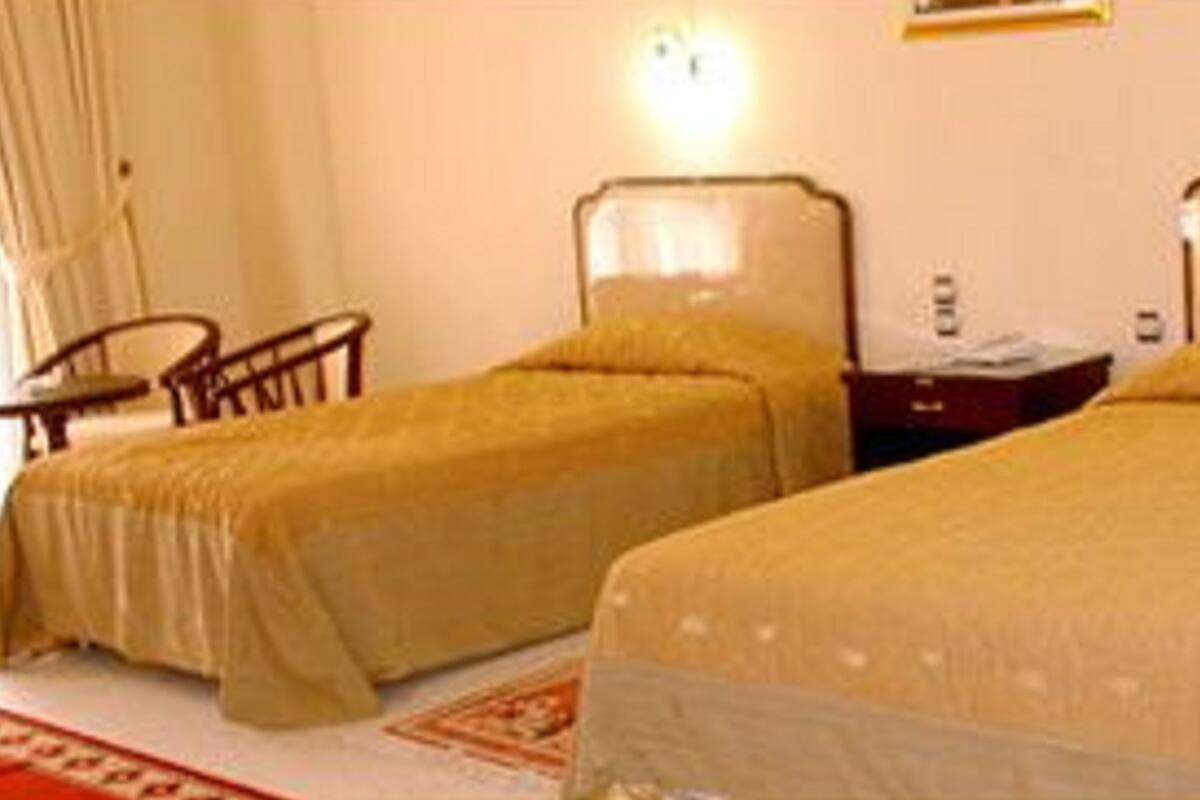 Two single beds with headboards, a nightstand, a chair, and a red carpet.