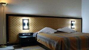 A hotel room with a checkered floor, a bed with a striped blanket, two bedside tables, and a wall-mounted light fixture. - Majestic Annaba (Annaba)