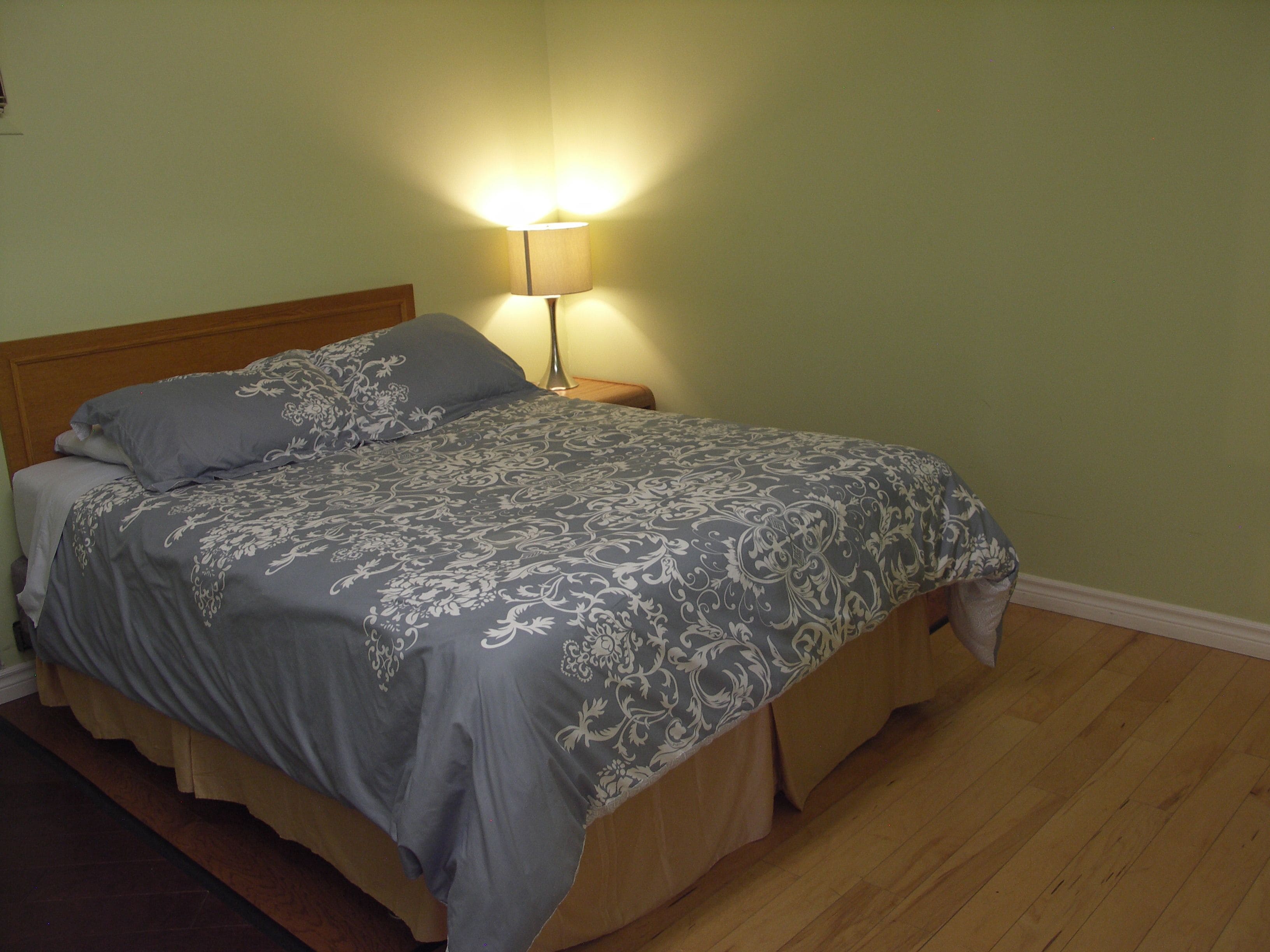A bed with a patterned bedspread, a nightstand with a lamp, and wooden flooring.