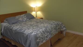 A bed with a patterned bedspread, a nightstand with a lamp, and wooden flooring.