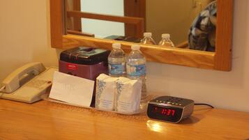 A hotel room counter with a telephone, a minibar, bottled water, a clock displaying 1:37, and a note labeled "TPS".