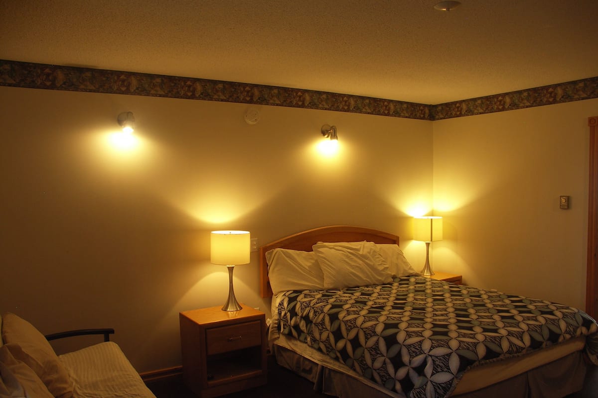 A hotel room with a bed, two bedside lamps, a nightstand, and a wall clock.