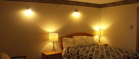 A hotel room with a bed, two bedside lamps, a nightstand, and a wall clock.