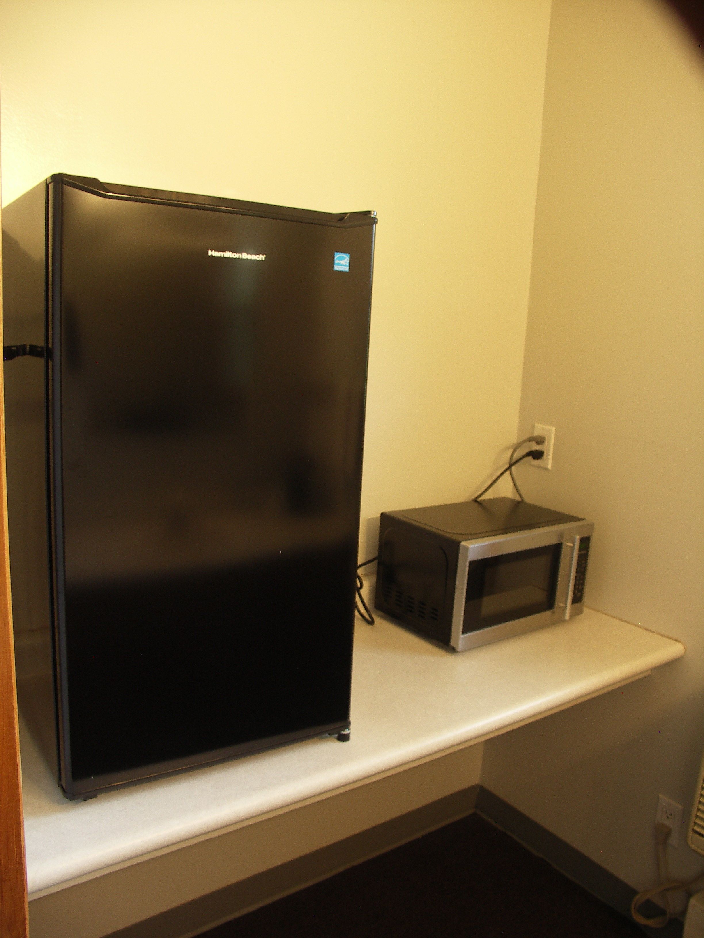A black refrigerator and a microwave on a white countertop in a kitchen.