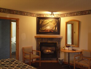 Una habitación con chimenea, dos sillones, una mesa con artículos de aseo y un cuadro sobre la chimenea.