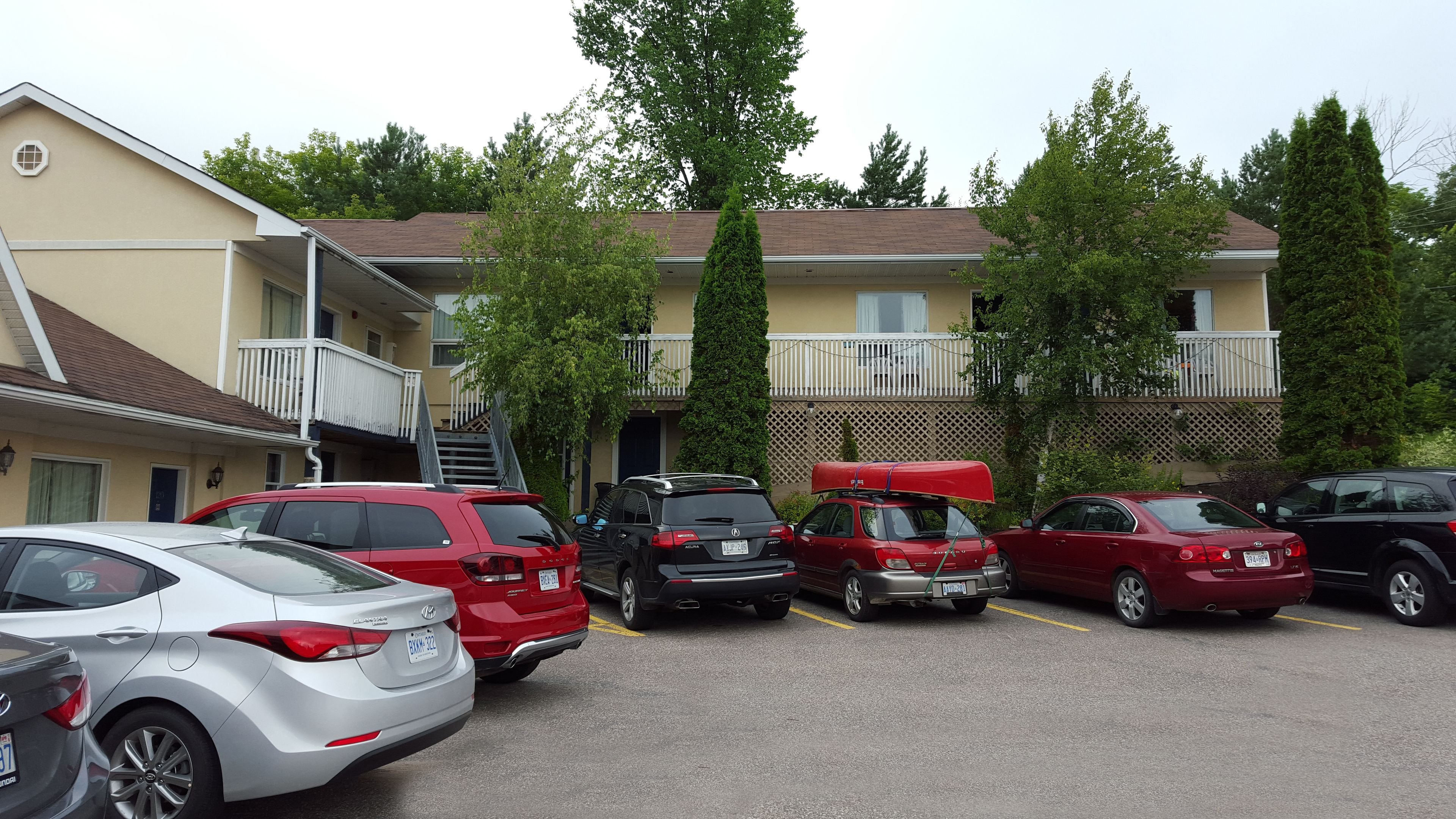 A parking lot with several cars, a building with a balcony, and a tree in the background.