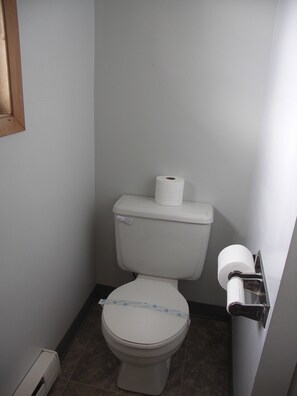 A small, compact bathroom with a toilet, a toilet paper holder, and a wall-mounted towel rack.