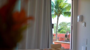Habitación de hotel con cama, ventana con cortinas y vista a una palmera, además de una pared roja en el exterior.