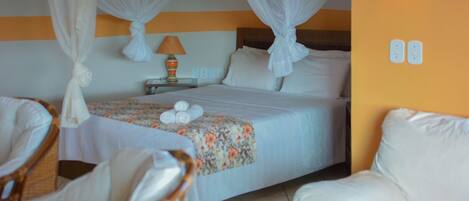A hotel room with a bed, two chairs, a nightstand with a lamp, and a wall with two light switches.