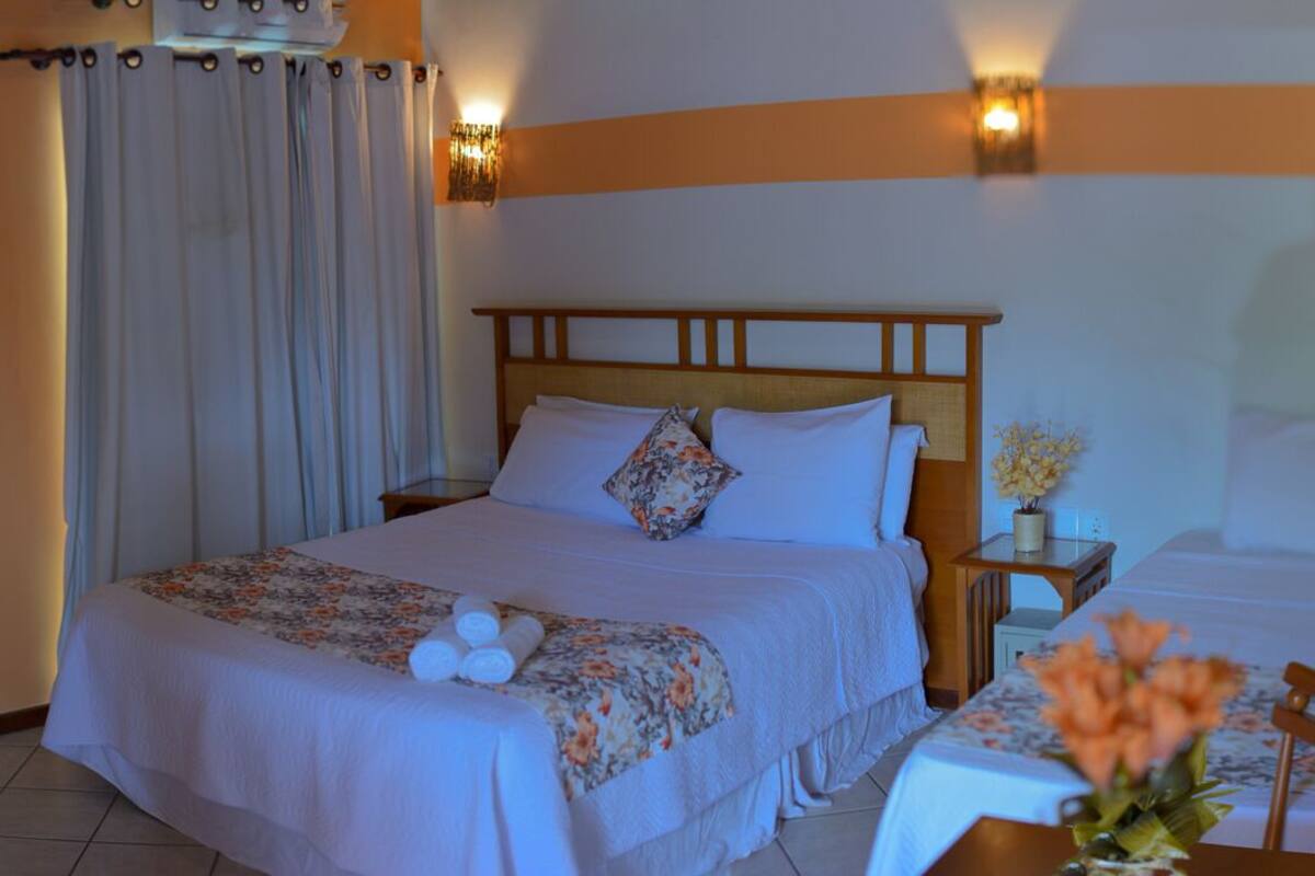 Ein Hotelzimmer mit Bett, Nachttisch, Tisch mit Blumen und Vorhang.