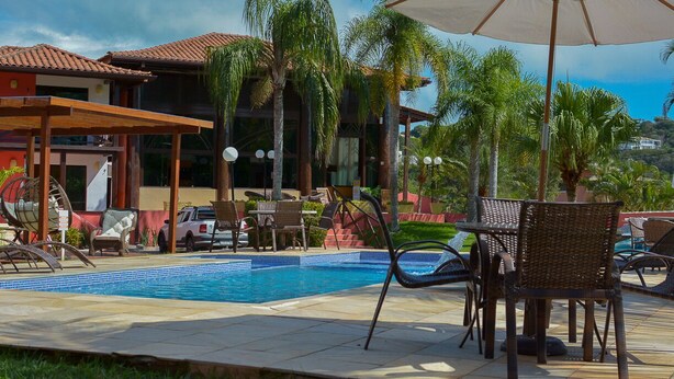 Un área de piscina con sillas de descanso, una sombrilla y un edificio con techo de tejas.