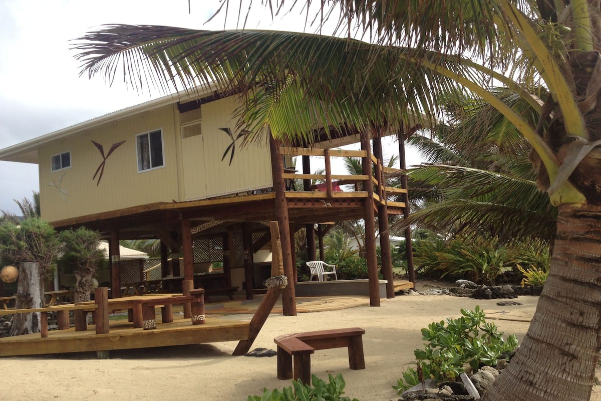 Ein Gebäude direkt am Strand mit einer Holzterrasse, einem überdachten Sitzbereich und einer Palme.