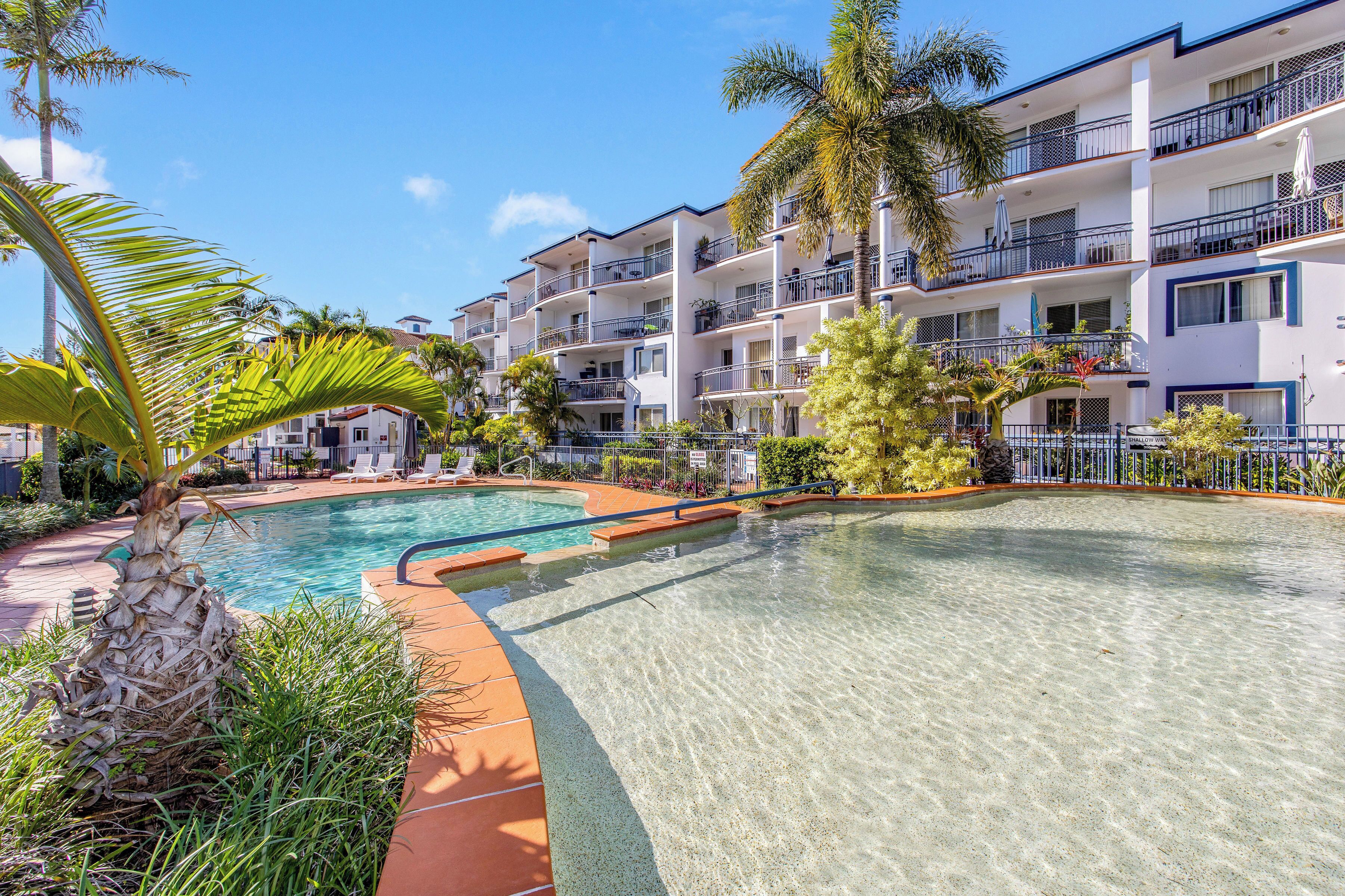A hotel with a swimming pool, palm trees, and balconies.