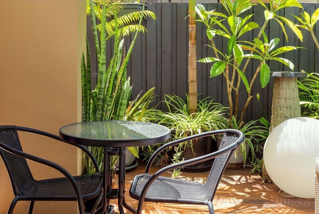 A patio with a round table and two chairs, surrounded by potted plants and a wooden fence.