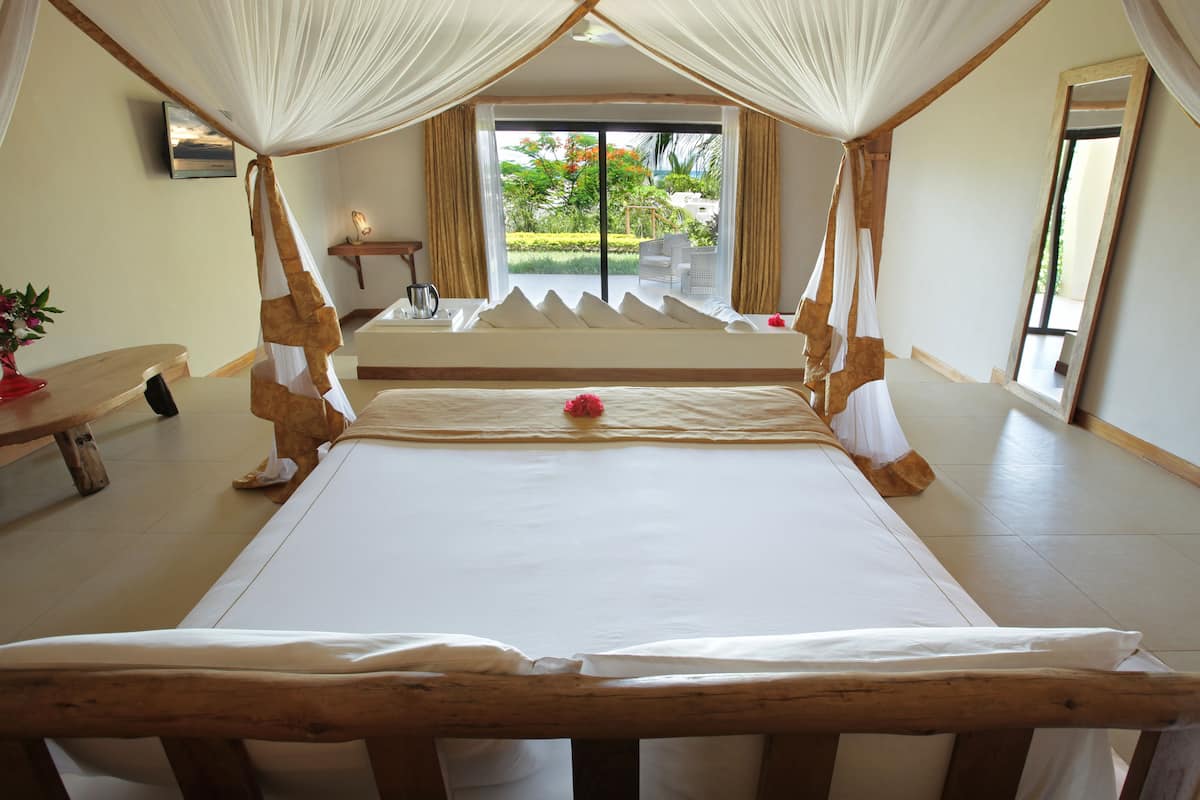 A spacious bedroom with a large bed, a wooden headboard, and a view of the garden through a sliding glass door.