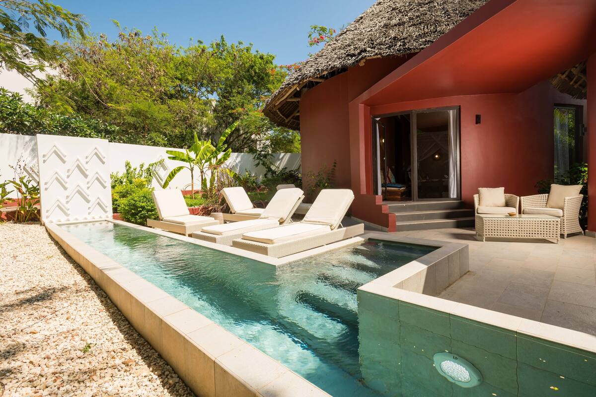 A swimming pool with lounge chairs, a covered patio area, and a building with a red exterior.