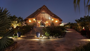 Um resort com um edifício de telhado de palha, um caminho pavimentado e paisagismo bem iluminado.