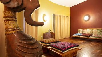Una stanza con una scultura di elefante in legno, un letto con cuscini a motivi, una panca di legno e un divano con cuscini.