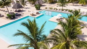 Um resort com piscina, praia e edifícios com telhado de palha.