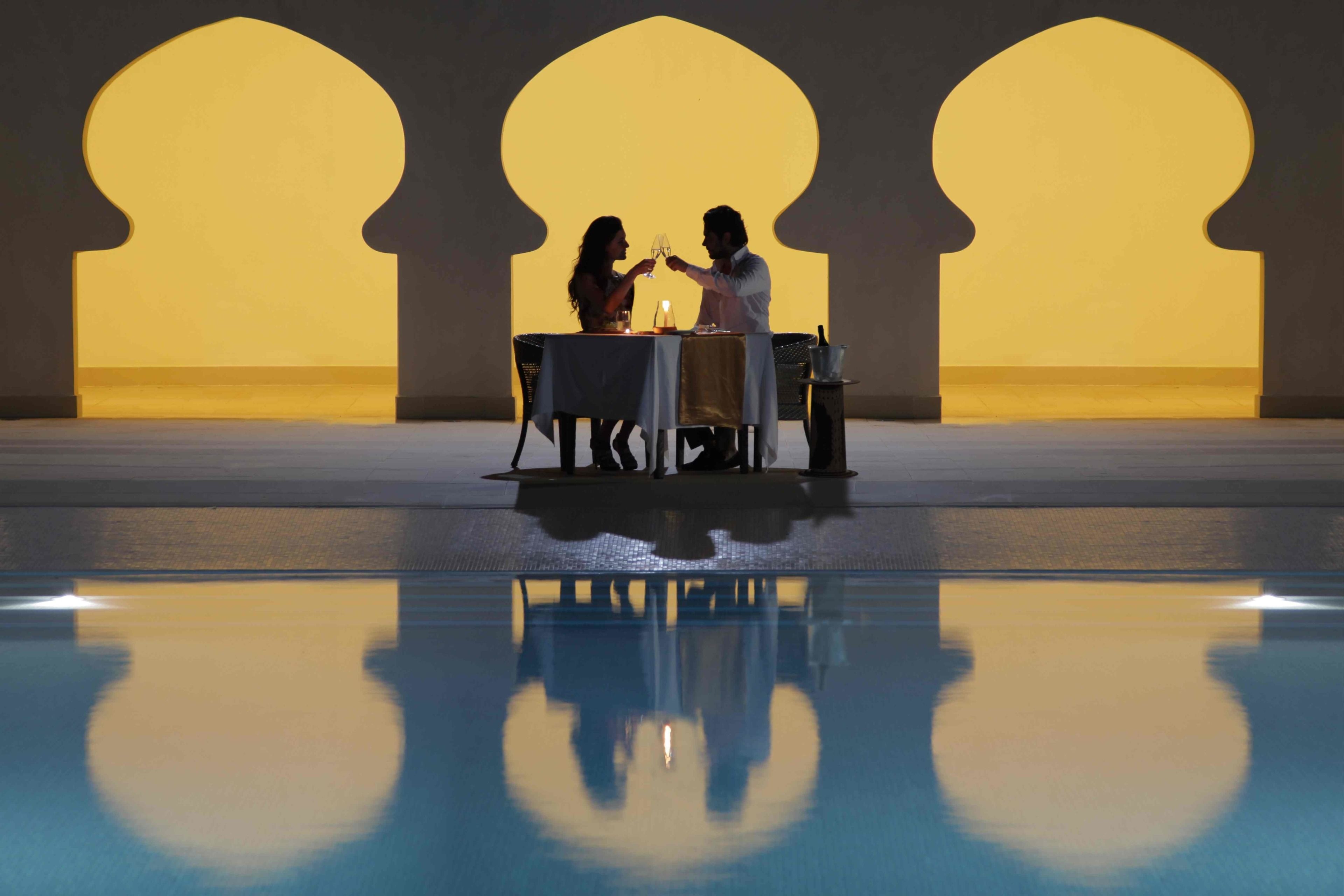 A dining area with a pool in the foreground and a large arched doorway in the background.