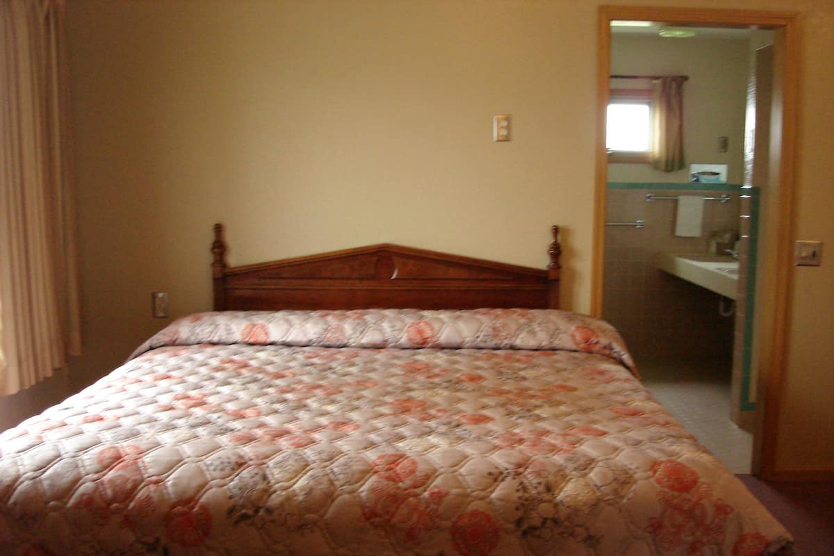 A bedroom with a wooden bed, a floral bedspread, and a view of a bathroom through an open door.