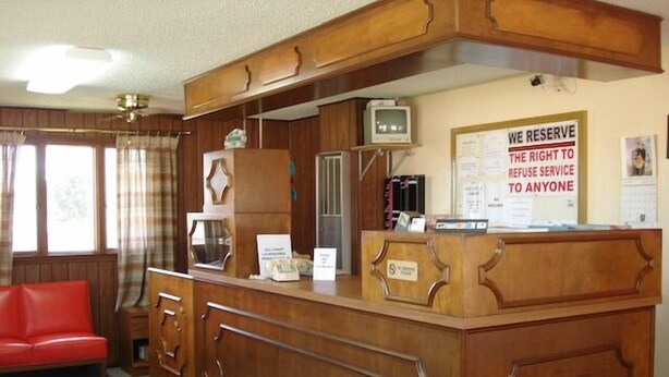 A reception area with a wooden counter, a red couch, and a sign stating "WE RESERVE THE RIGHT TO REFUSE SERVICE TO ANYONE".