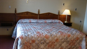 A standard hotel room with a large bed, a bedside lamp, and a wooden headboard.