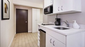 A compact kitchen with white cabinets, a microwave, a coffee maker, and a sink.
