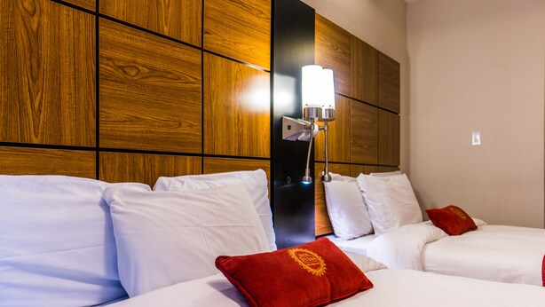 A hotel room with two beds, white bedding, a red pillow, and a wall-mounted light fixture.