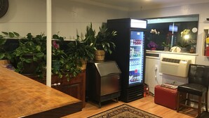 A living room with a wooden table, a black refrigerator, a red ottoman, and a patterned rug. - Country Manor Motel Watkins (Watkins)