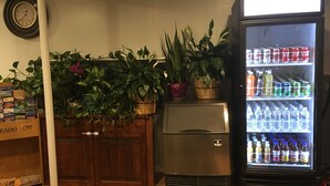 A room with a refrigerator stocked with beverages, a clock on the wall, and various potted plants. - Country Manor Motel Watkins (Watkins)
