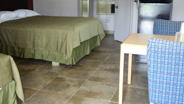 A room with a bed, a table, a chair, a television, and a window with curtains. - Palm City Motel (Fort Myers)