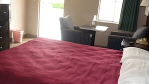 A hotel room with a large bed, a small table, two chairs, a dresser, and a window with curtains. - Palm City Motel (Fort Myers)