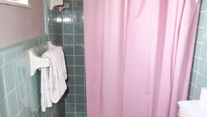 A small bathroom with a toilet, a shower with a pink curtain, and a towel rack with towels. - Palm City Motel (Fort Myers)