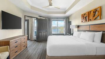 Quarto de hotel com cama, escrivaninha, televisão, ventoinha no teto e vista para o exterior.
