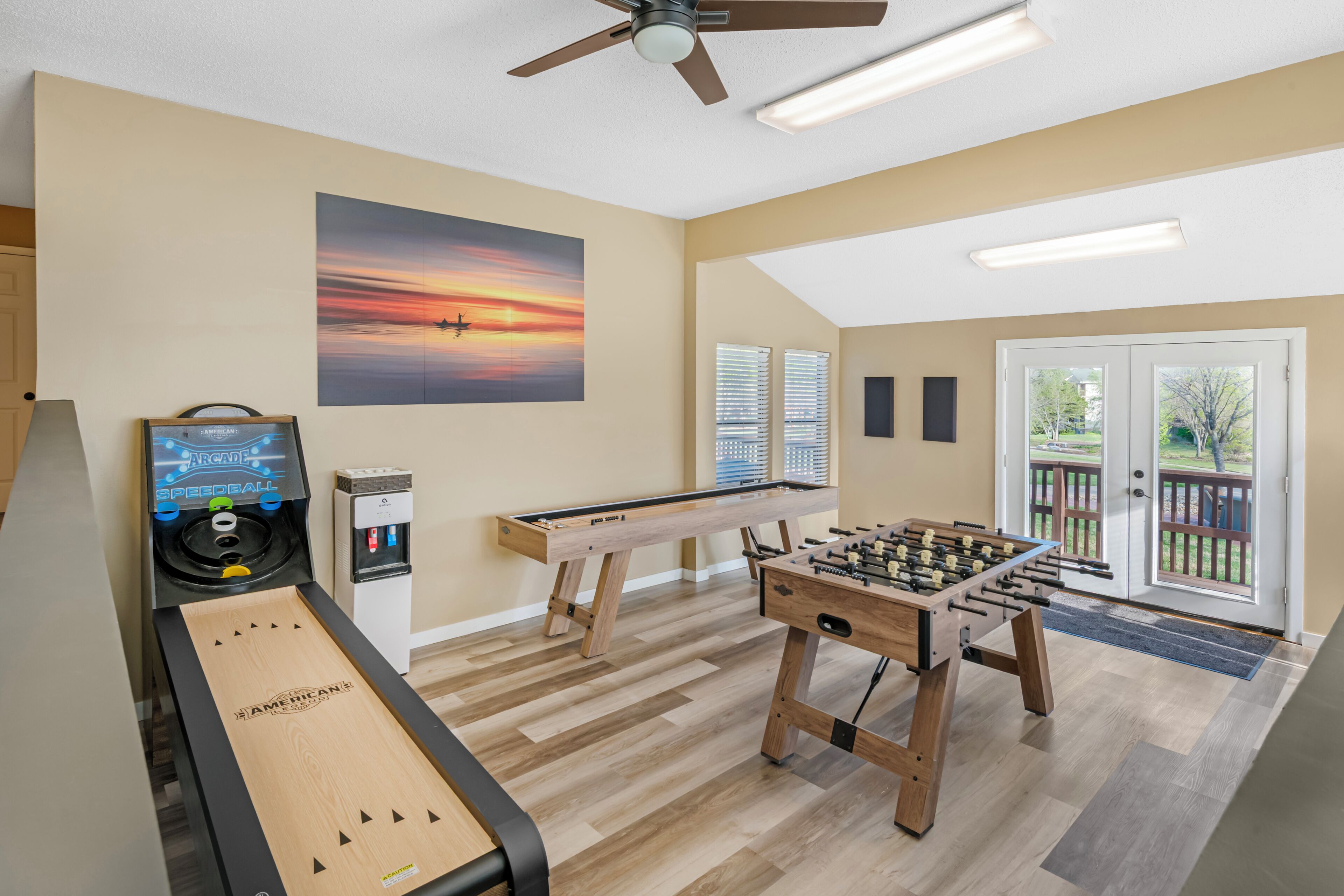 Una habitación con mesa de fútbol de mesa, mesa de billar y una mesa de fútbol de mesa con un cuadro de atardecer en la pared.