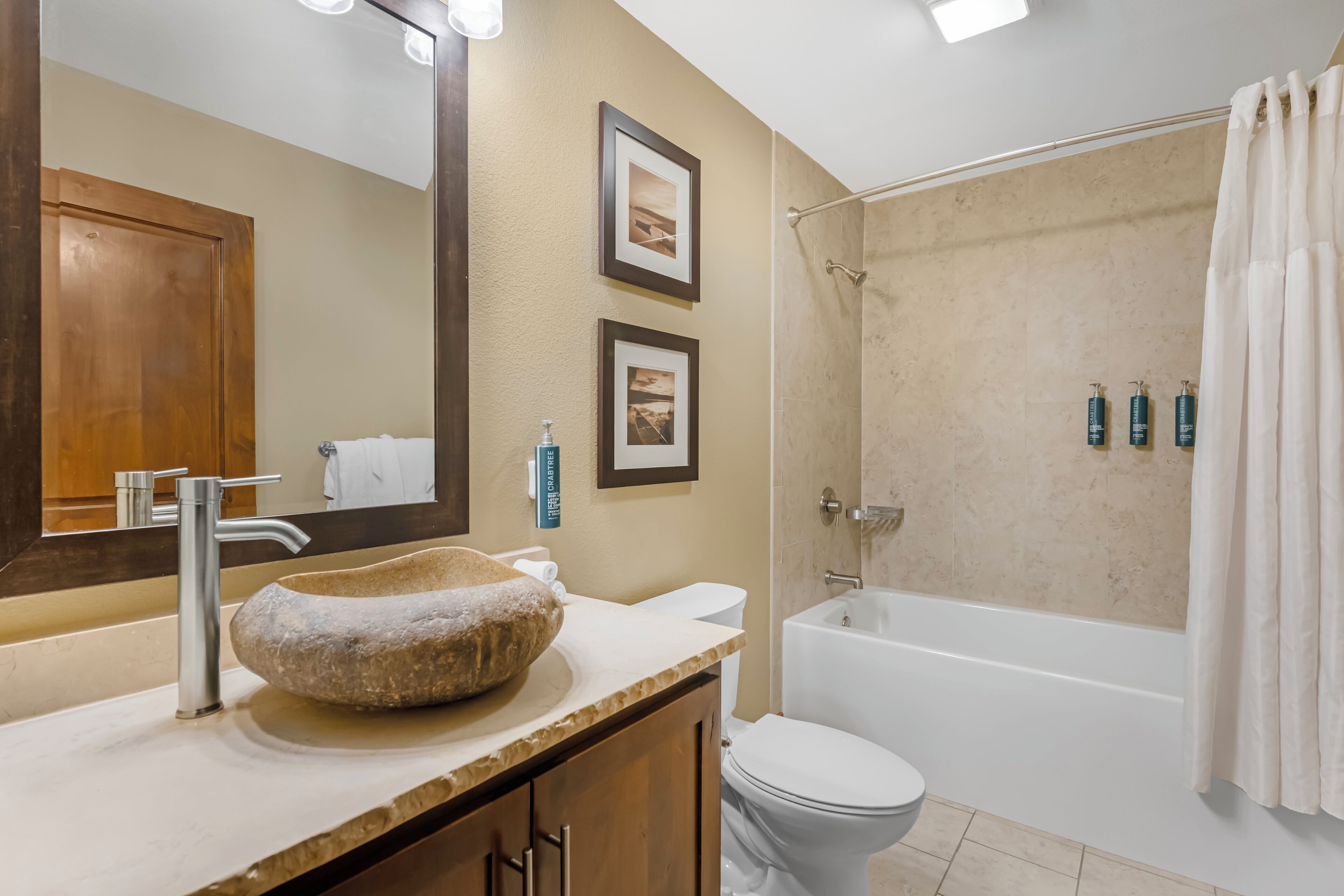 A bathroom with a stone basin sink, a toilet, a bathtub, and a shower curtain.