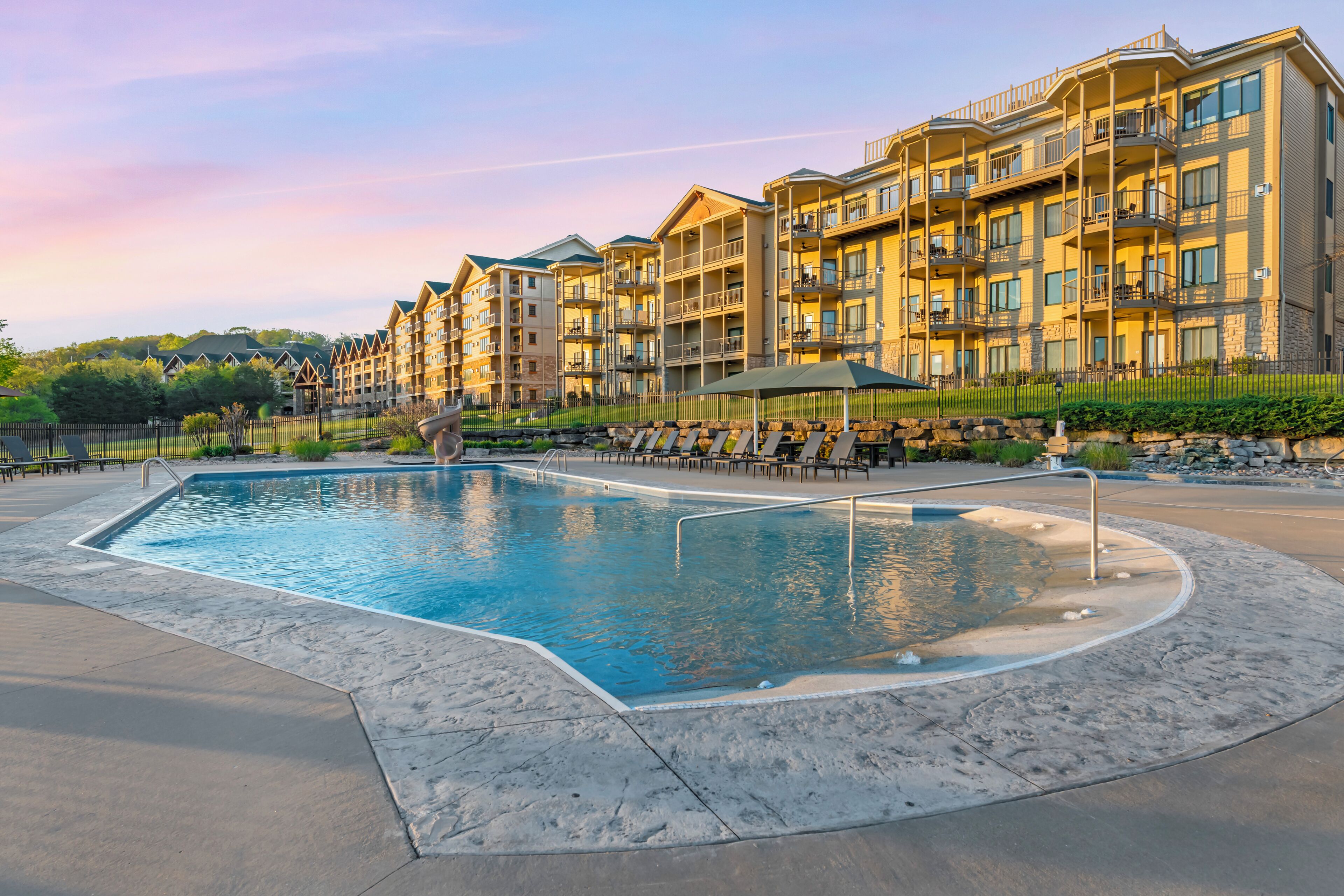 A swimming pool with lounge chairs and a building with balconies.