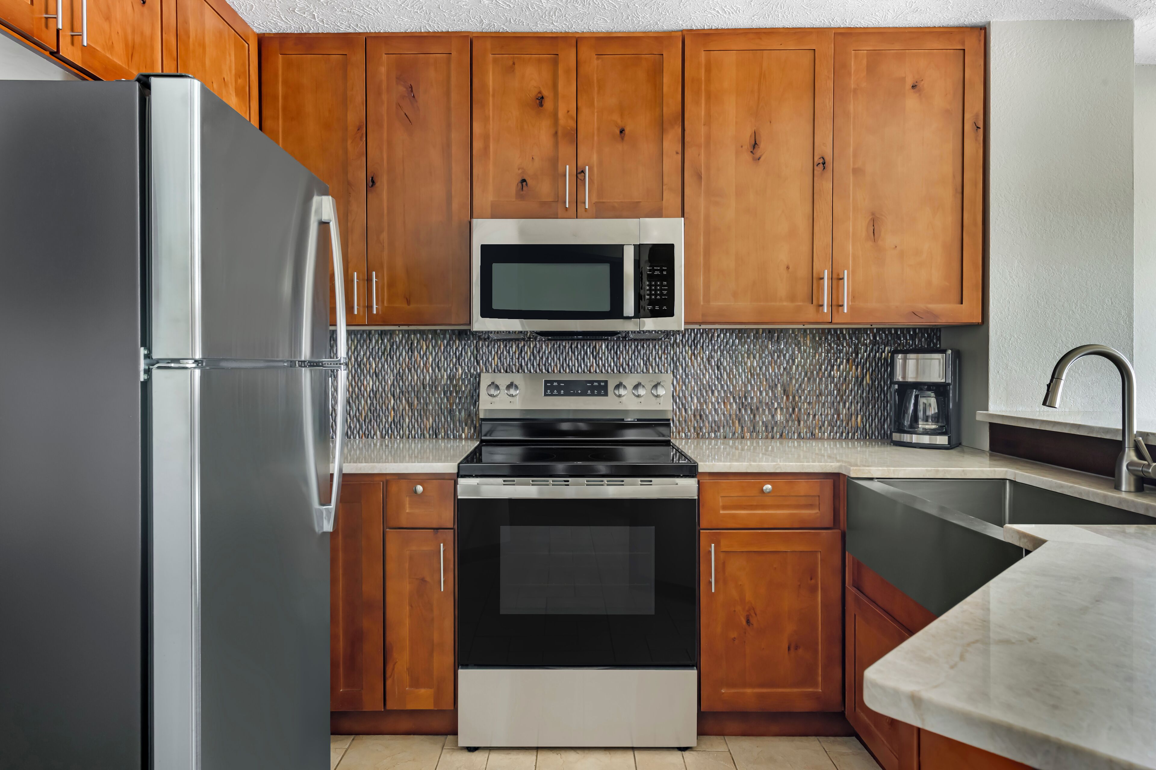 A kitchen with wooden cabinets, a stainless steel refrigerator, a microwave, an oven, and a sink.