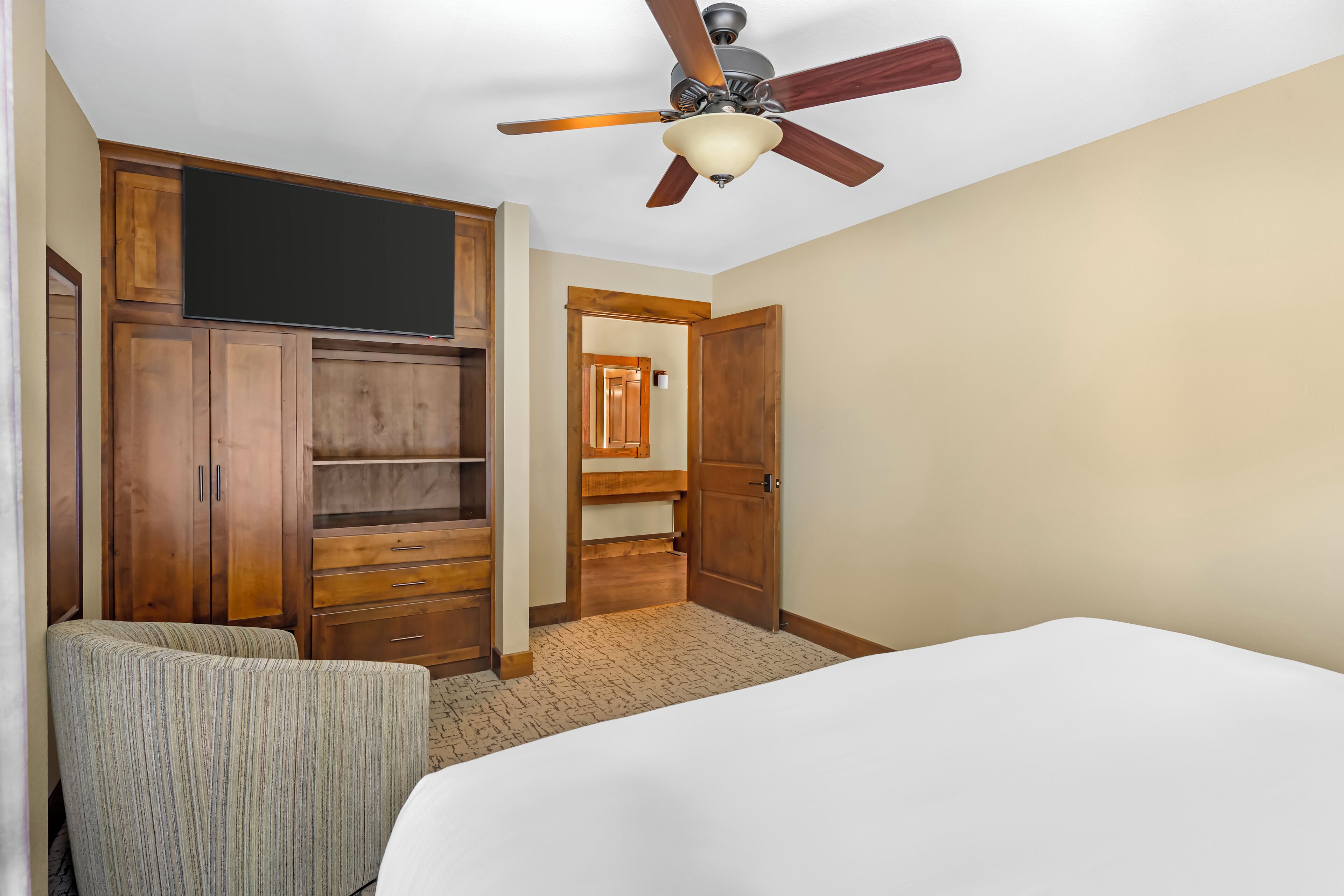Un dormitorio con cama, ventilador de techo, armario de madera y televisor.