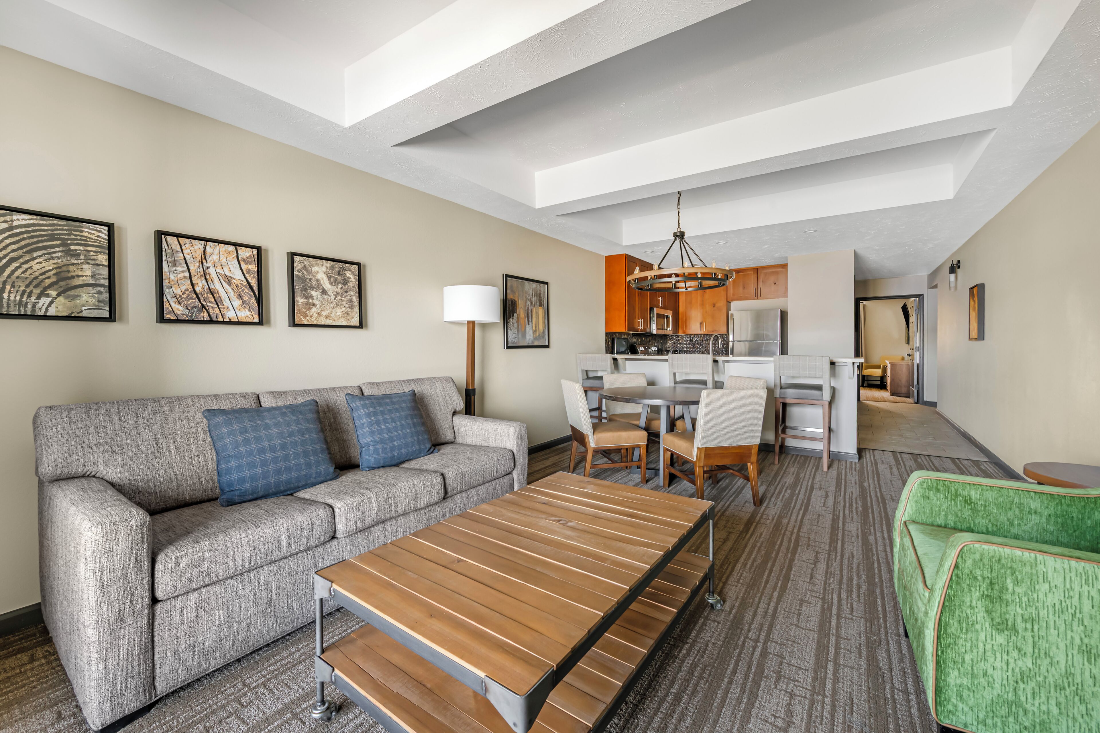 A modern hotel room with a sofa, a dining table, a kitchen area, and artwork on the walls.