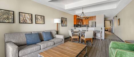 A modern hotel room with a sofa, a dining table, a kitchen area, and artwork on the walls.