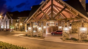 A hotel with a stone facade, wooden beams, and a red car parked in front.