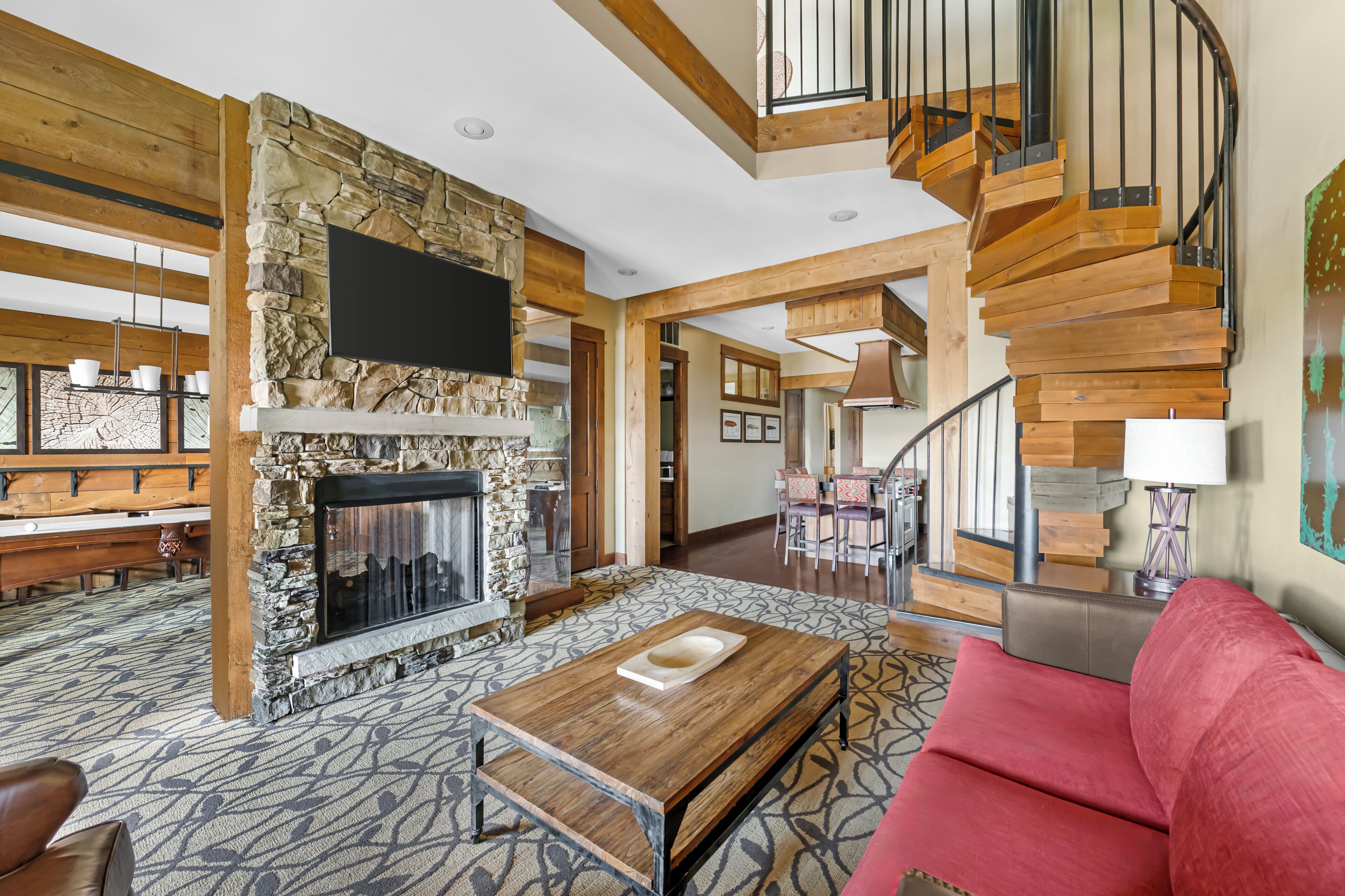 A spacious living area with a stone fireplace, a wooden staircase, and a red sofa.