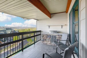 A covered balcony with a stone wall, a grill, and two wicker chairs.