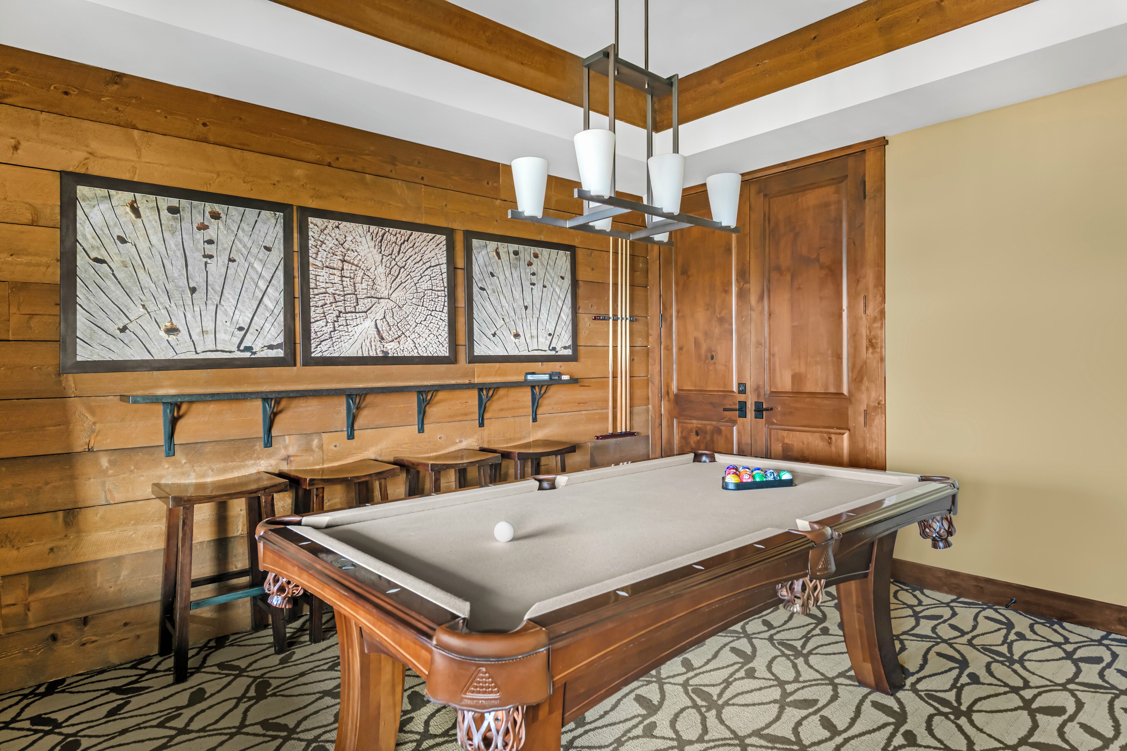 Une table de billard avec des tabourets, un mur en bois orné d’œuvres d’art et un meuble en bois.